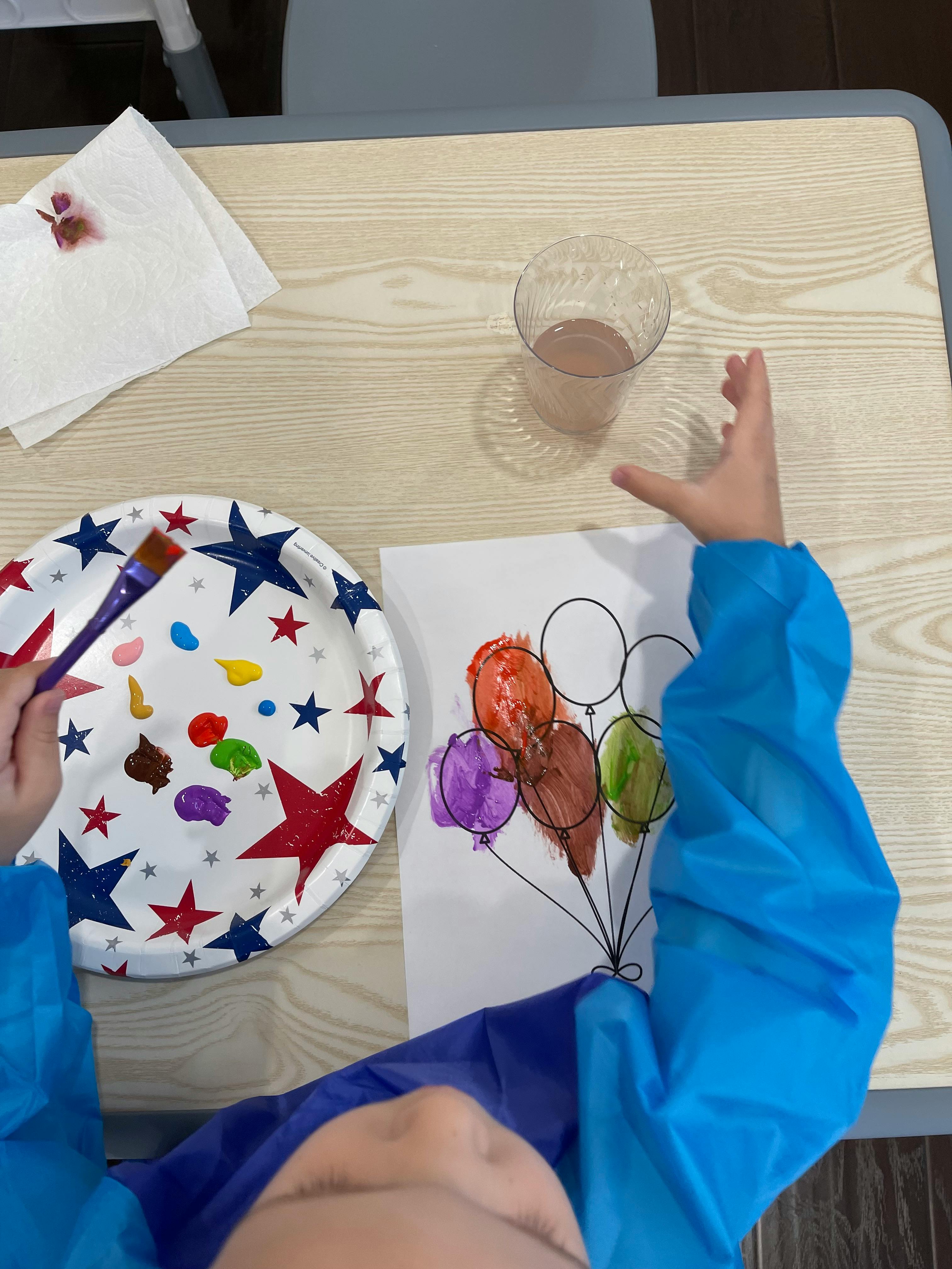 Child in an apron painting a balloon drawing on a table