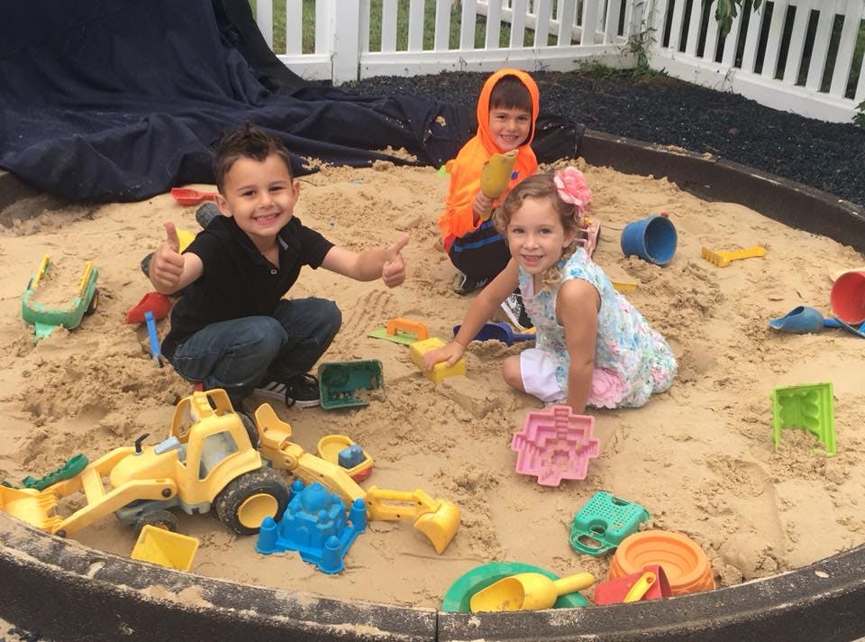 Three children playing in a sandbox with toys