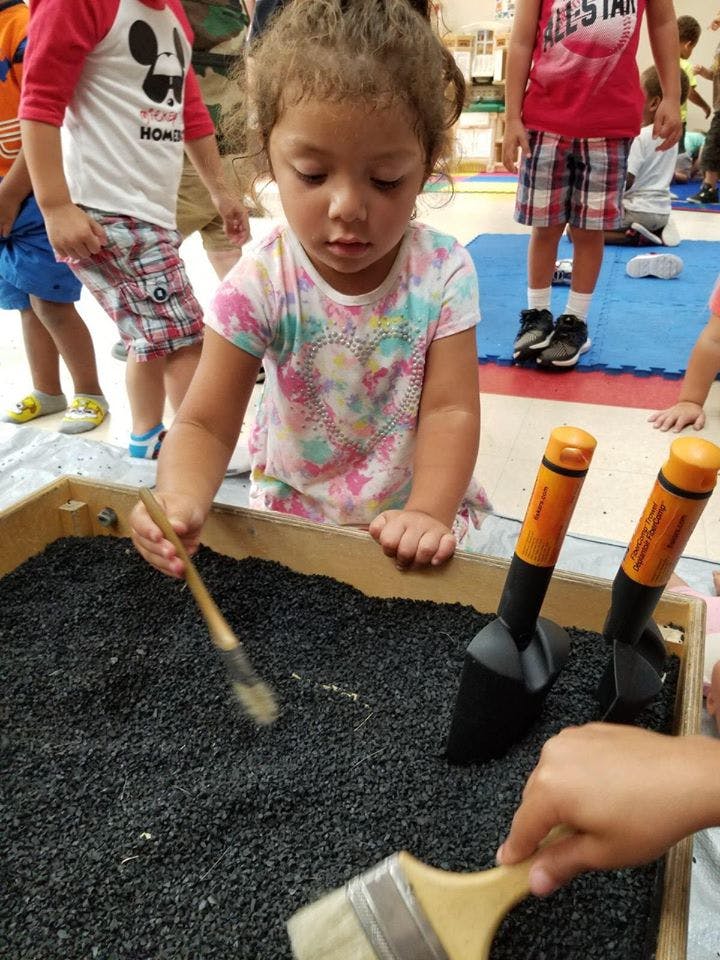 Child playing with brushes and shovels in a bin of black pebbles