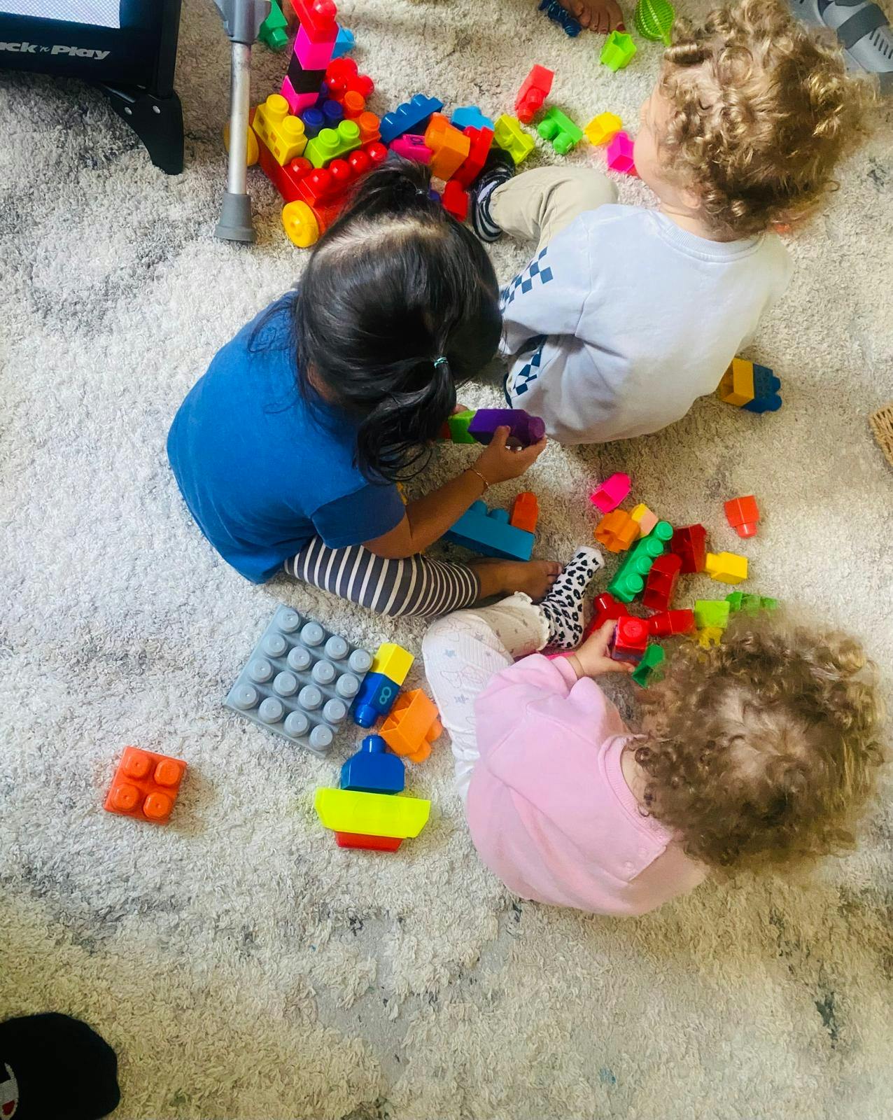 Three children playing with colorful building blocks on a rug