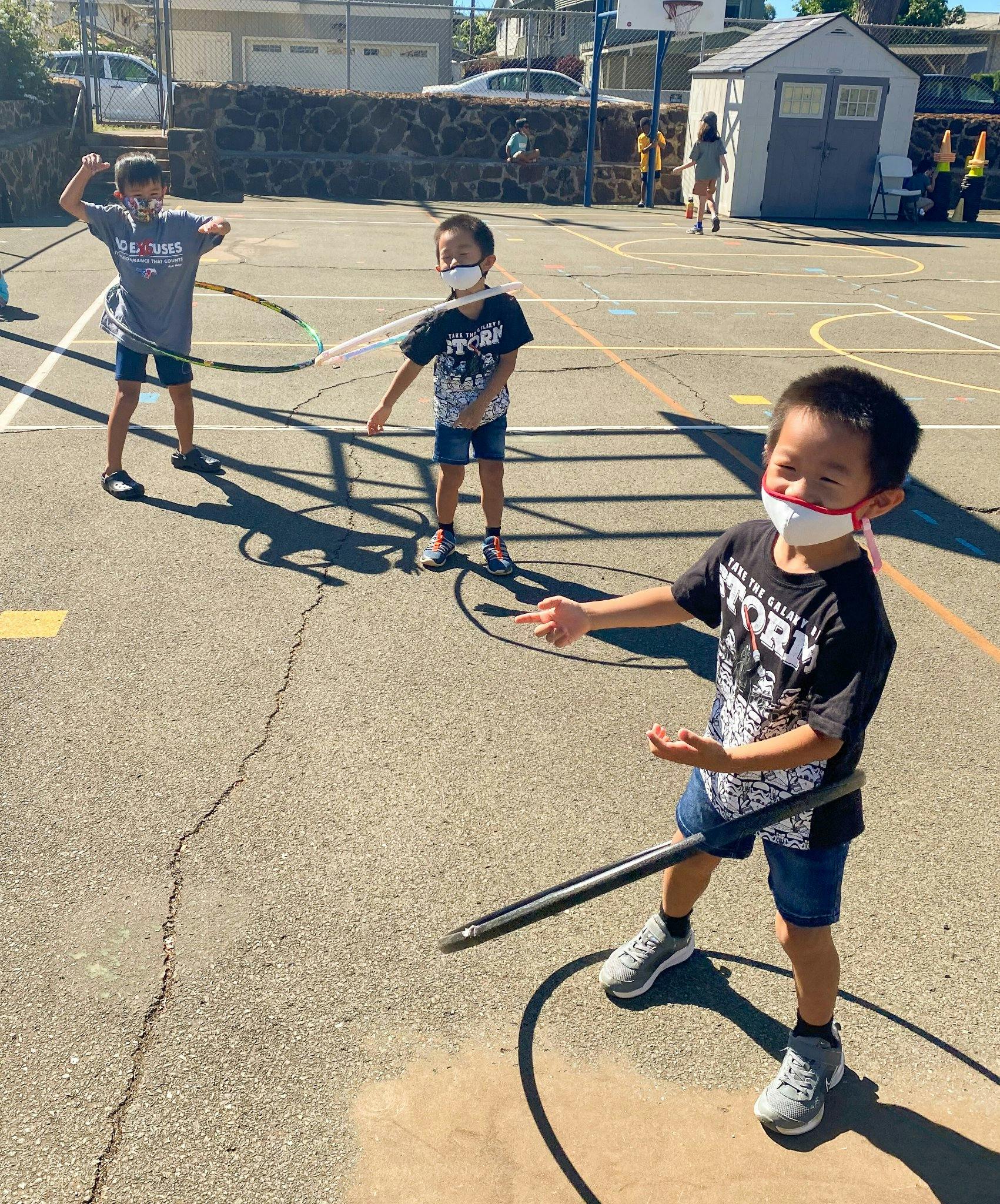 Three children playing with hula hoops on an asphalt court