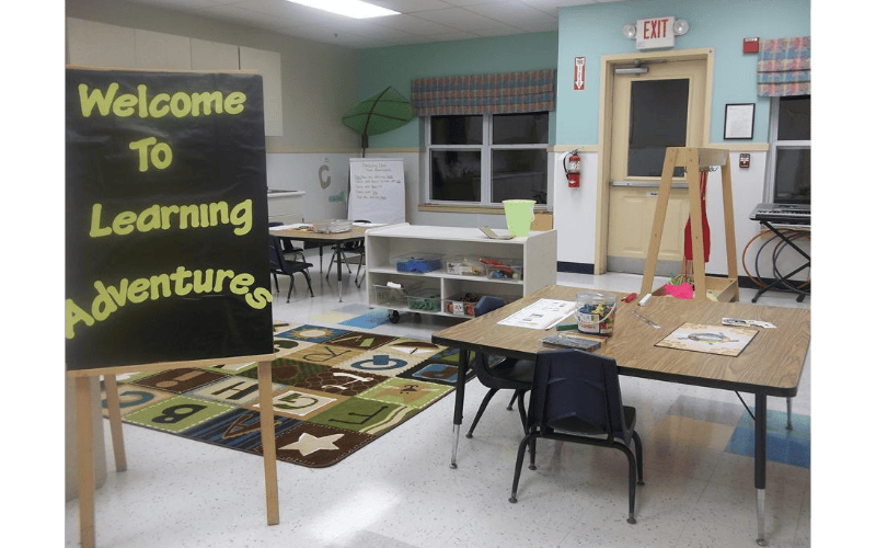 Classroom with "Welcome To Learning Adventures" sign and children's tables and chairs