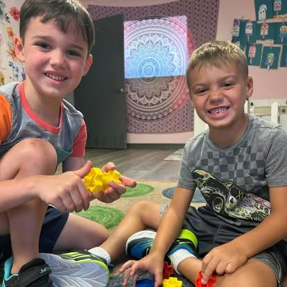 Two children sitting on the floor playing with colorful plastic building blocks