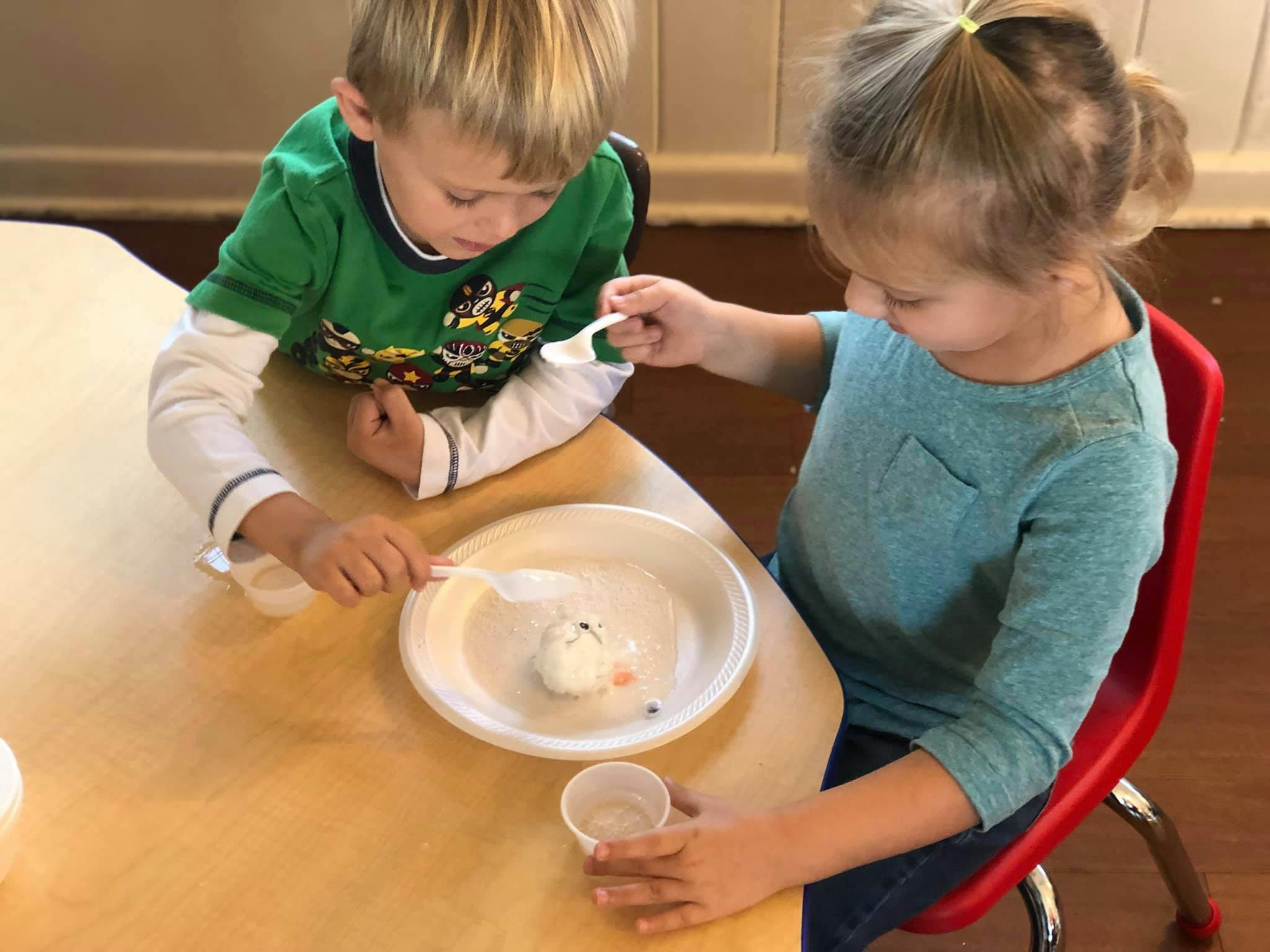 Two children at a table with spoons and a plate