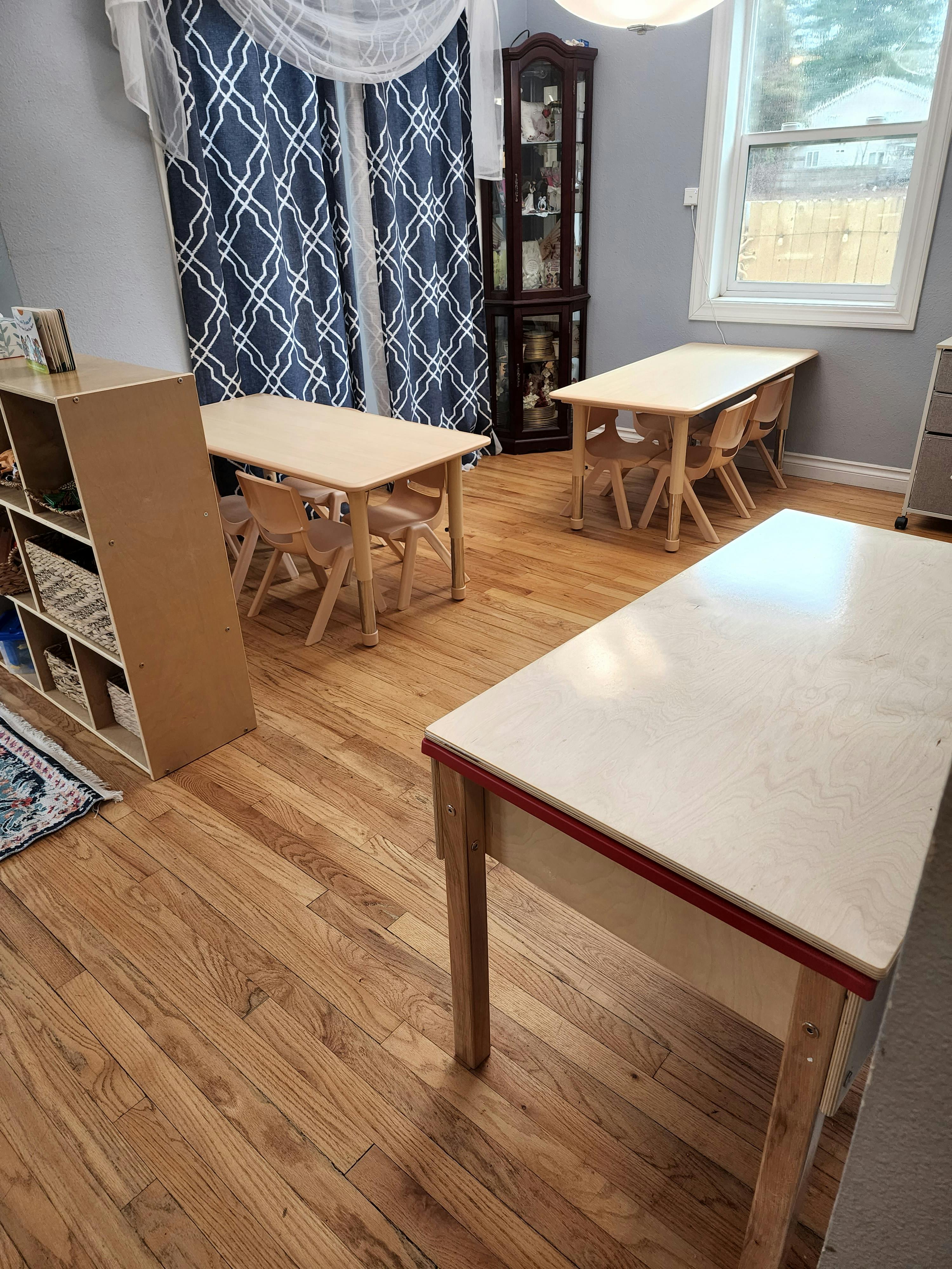 Classroom with small tables and chairs, a bookshelf, and patterned curtains