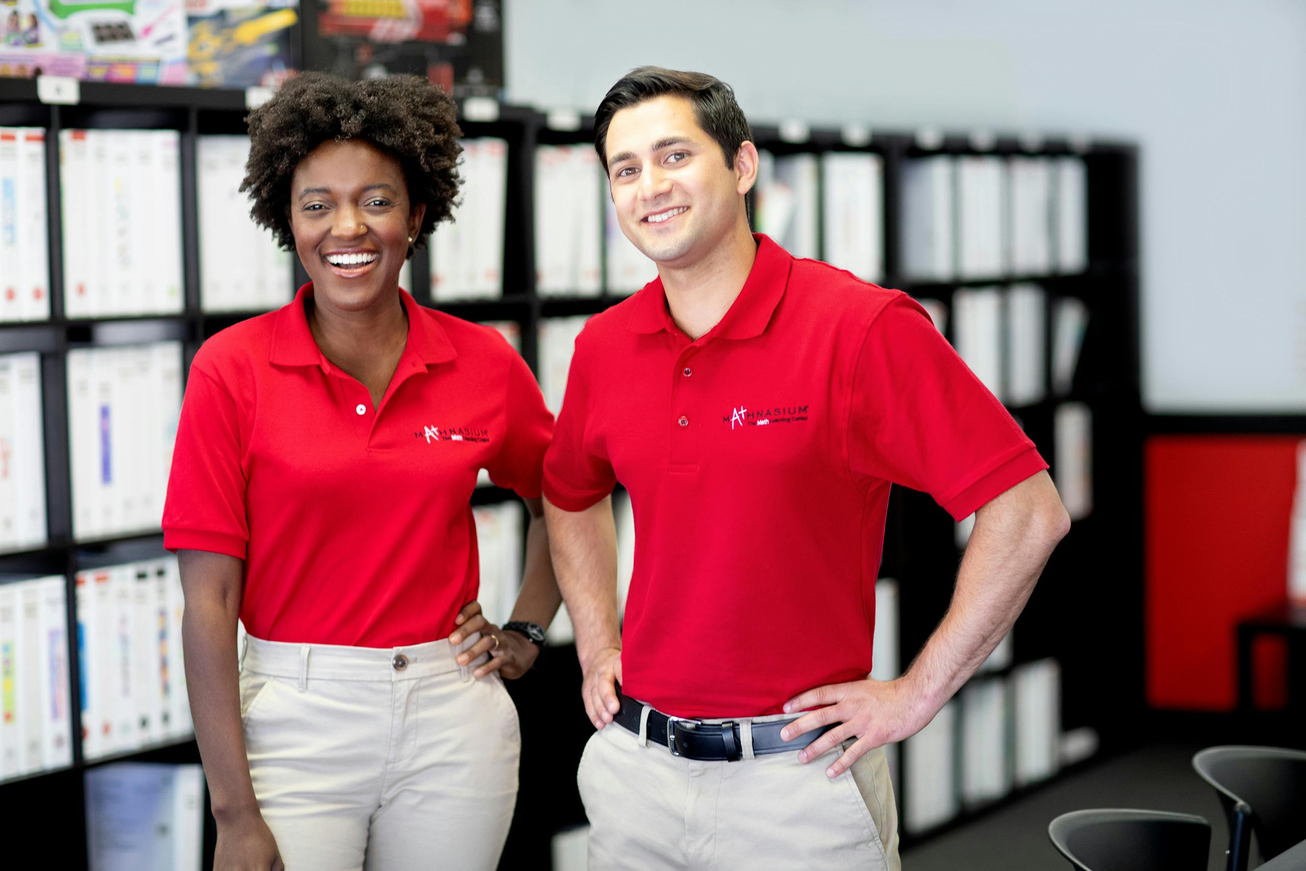 Two people in red polo shirts with Mathnasium branding standing in an office