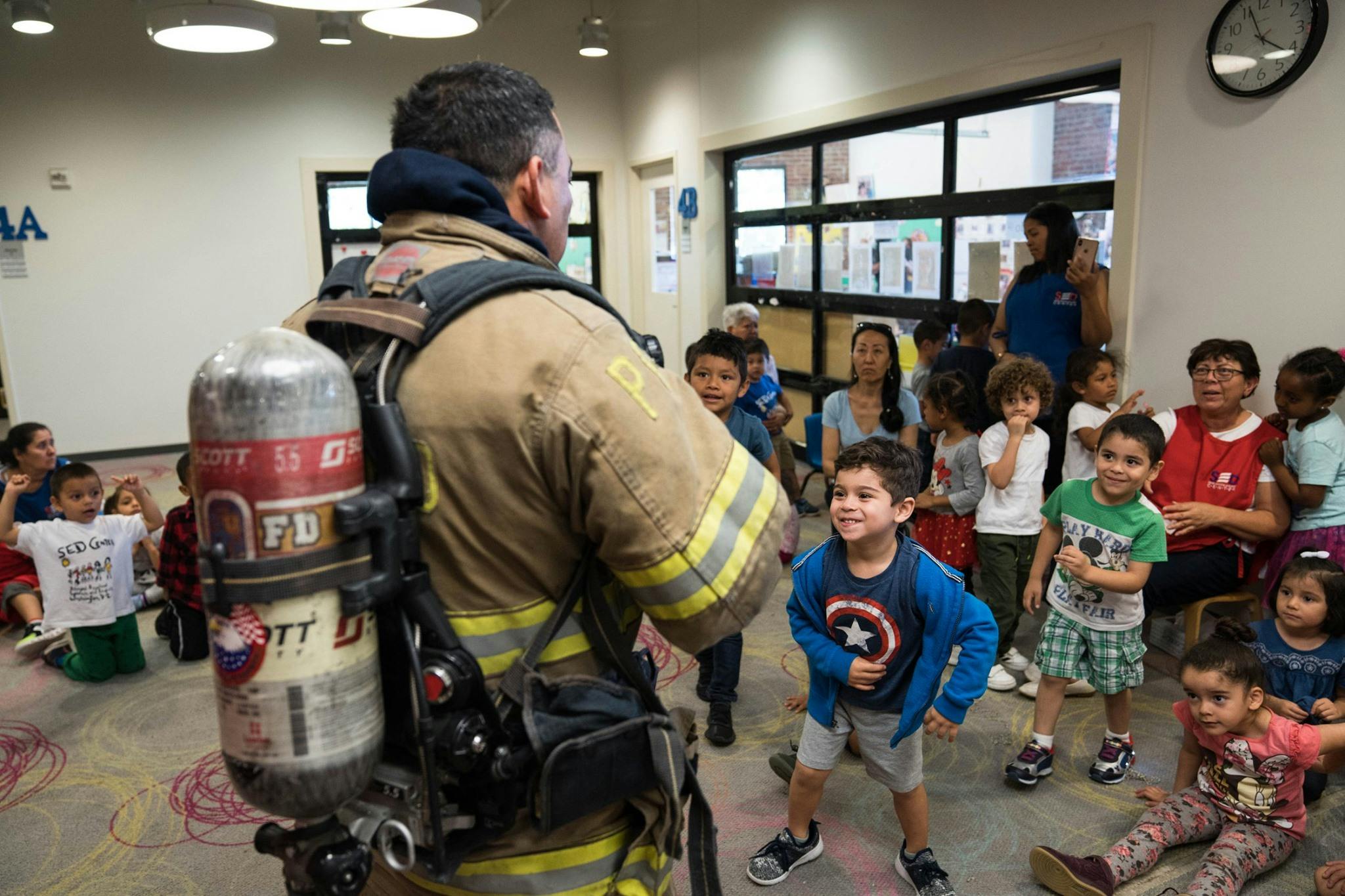 Firefighter in uniform with air tank talking to a group of children and adults