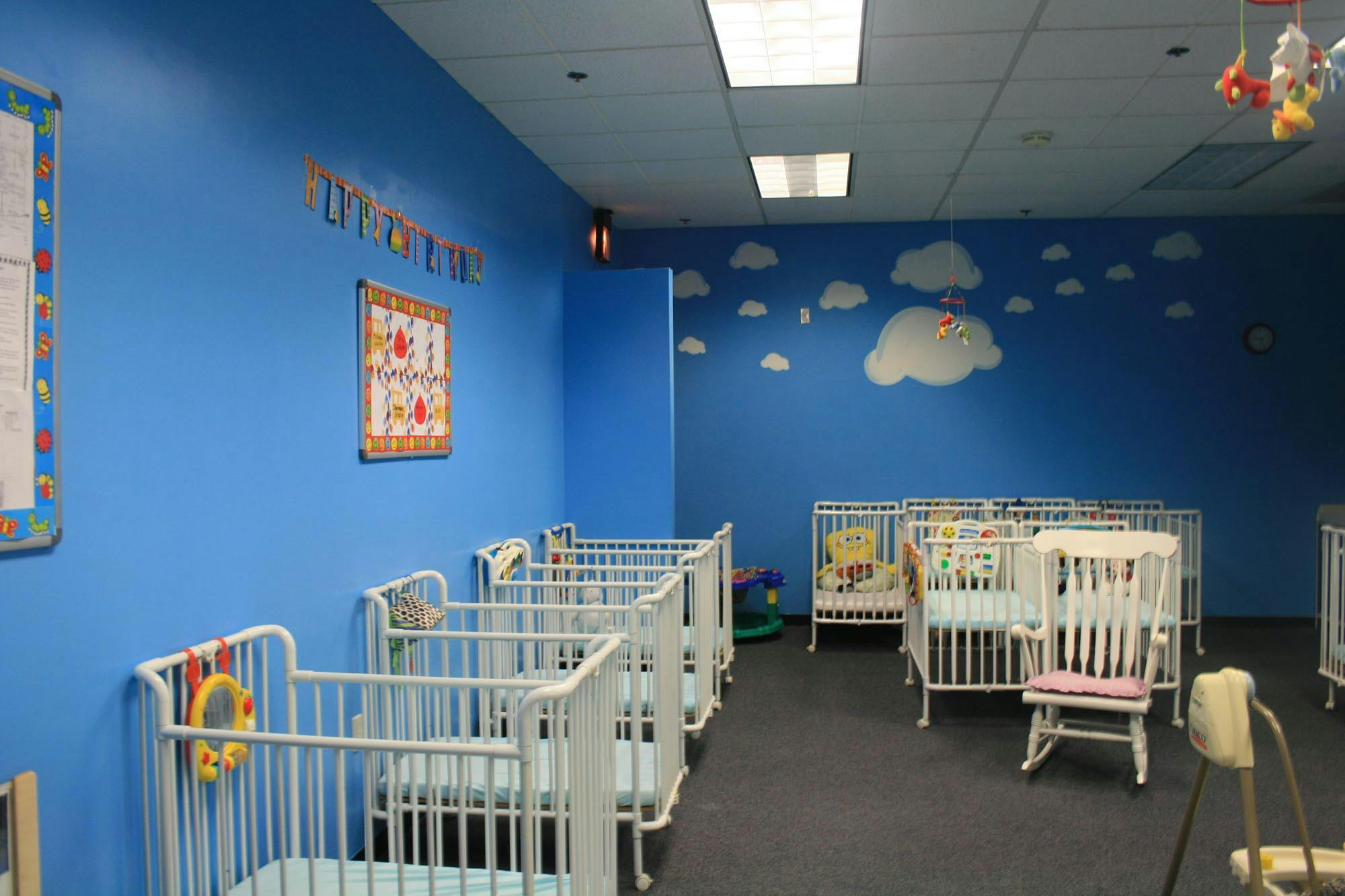 Nursery room with multiple white cribs and blue walls with cloud decals
