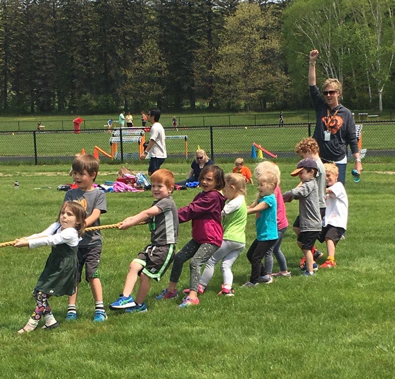 Children playing tug-of-war outdoors with an adult supervising