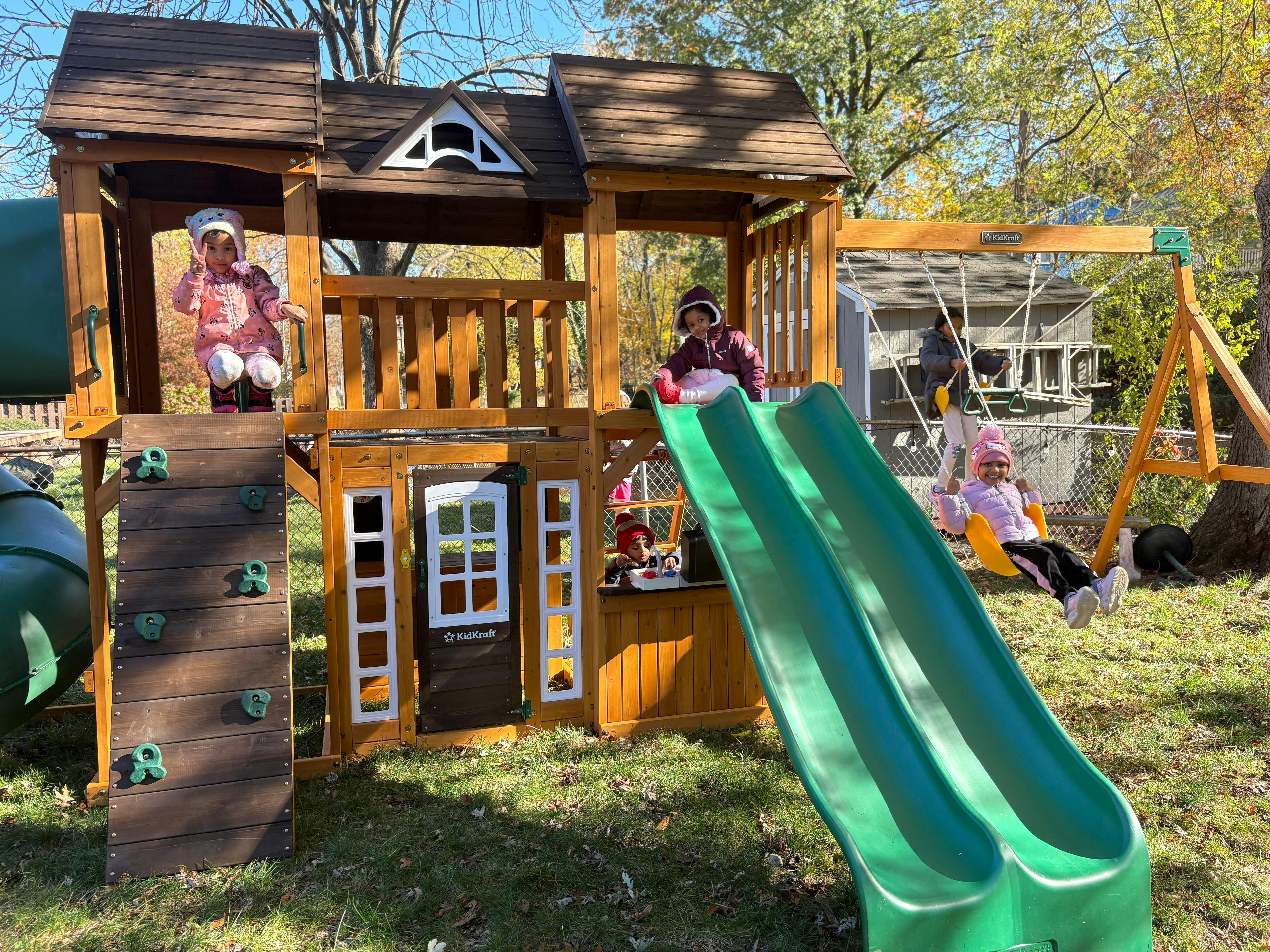 Children playing on an outdoor playset with slides, swings, and a climbing wall