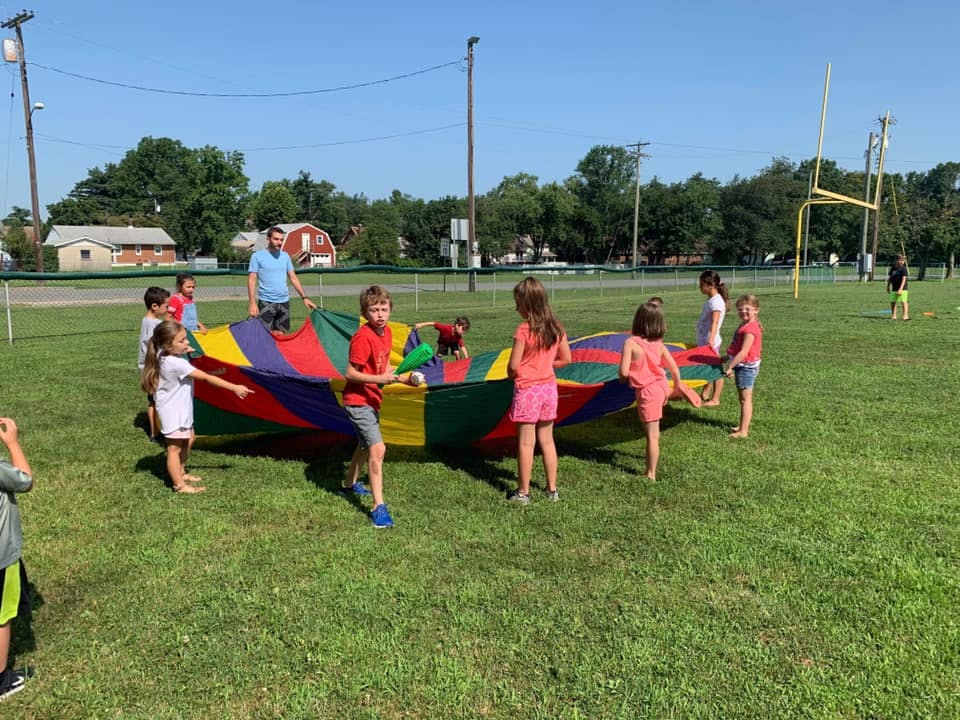 Children and an adult playing with a colorful parachute on a grassy field