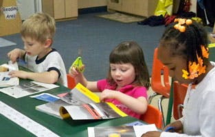 Three children working at a table in a classroom