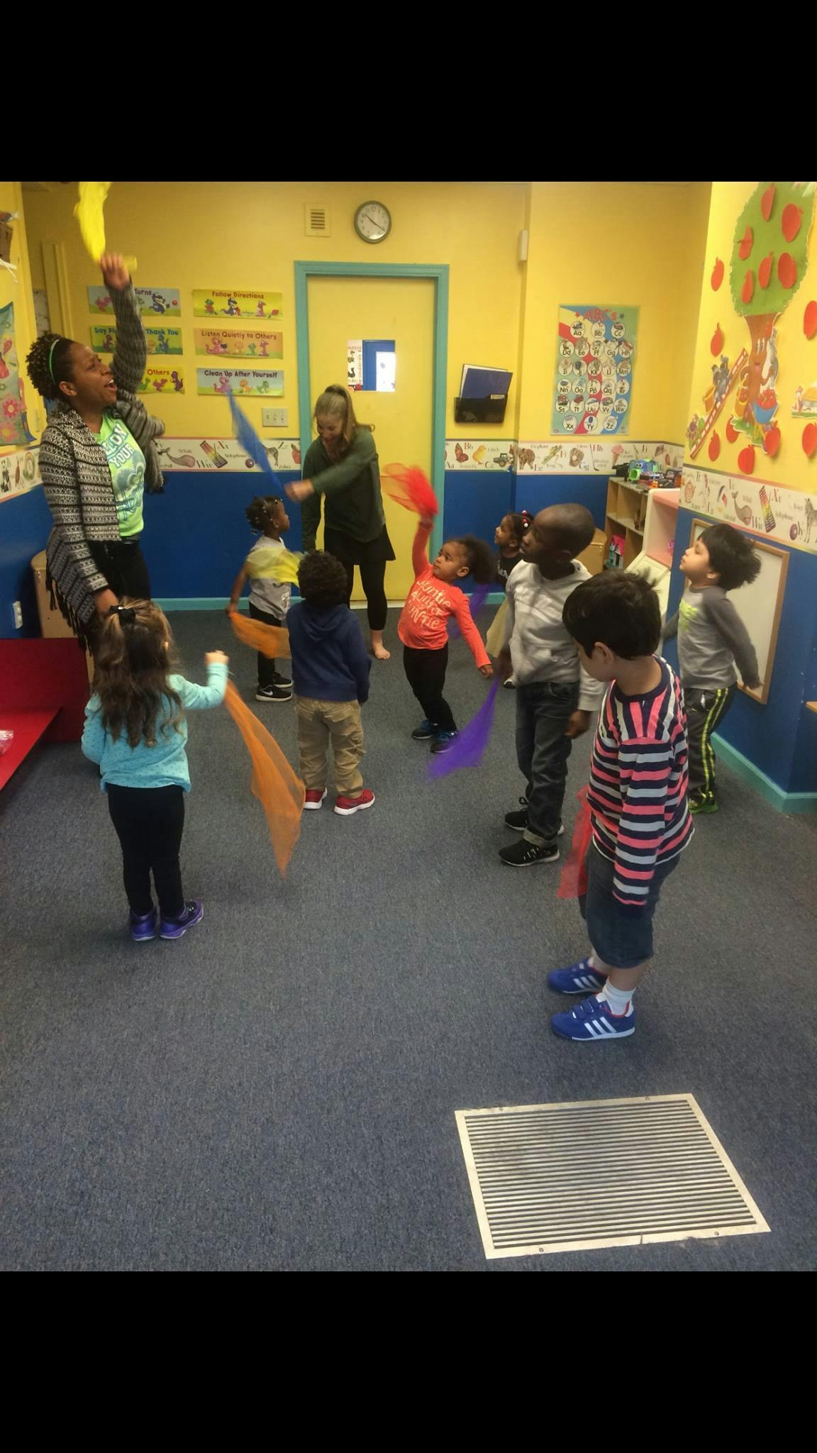 Adults and children in a classroom holding colorful scarves