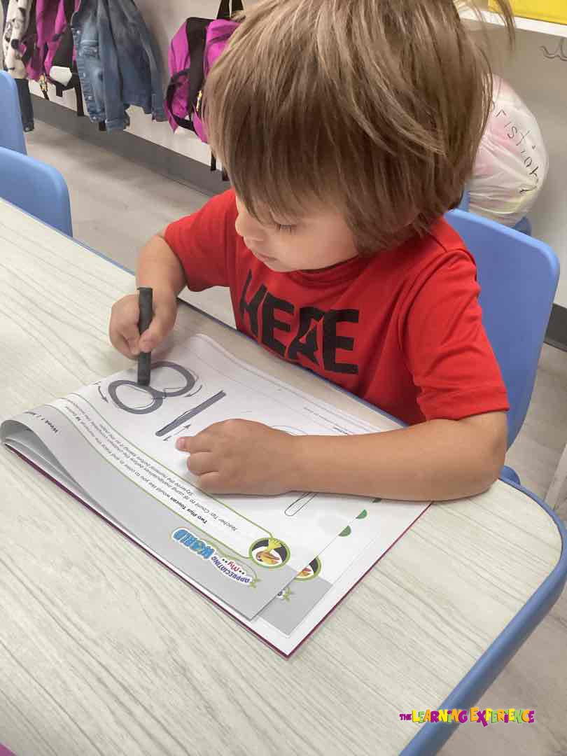 Child drawing the number 8 in a workbook at a desk
