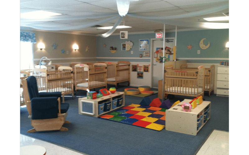 A room with several cribs, a rocking chair, and a colorful play mat