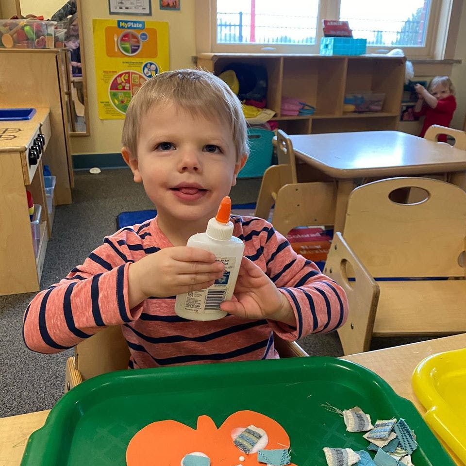 Child holding a bottle of glue in a classroom