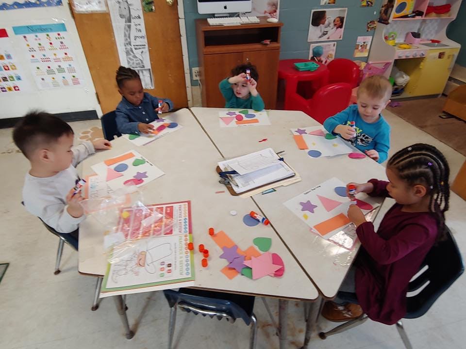 Four children sitting at a table doing crafts in a classroom