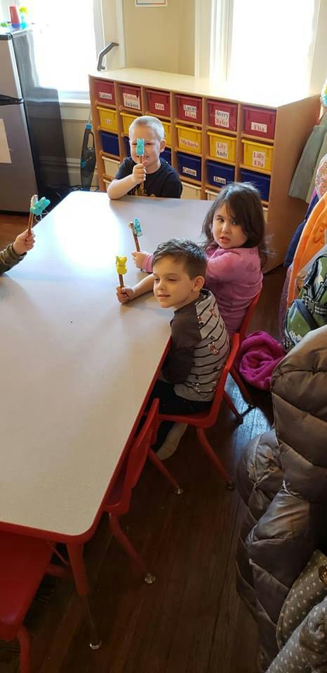 Children sitting at a table holding craft sticks with animal shapes