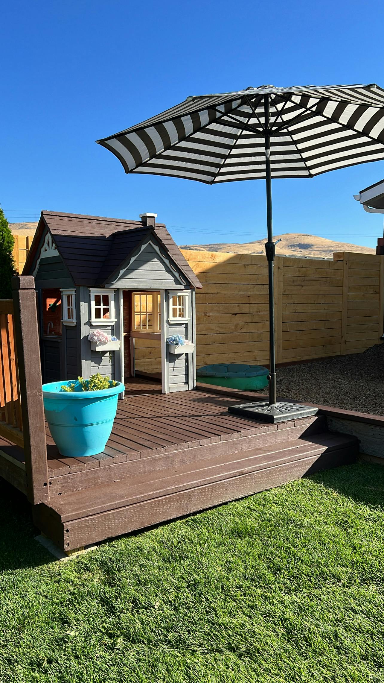 Playhouse on a deck with a striped umbrella and a planter