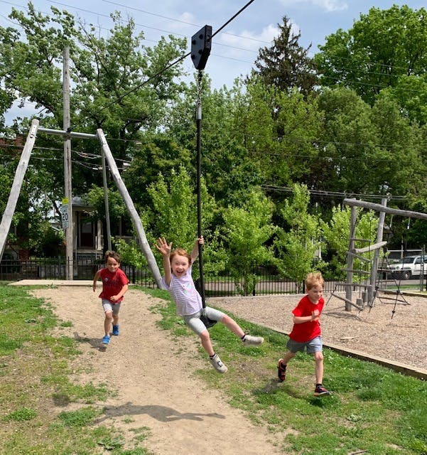 Child on a zip line with two children running on a playground