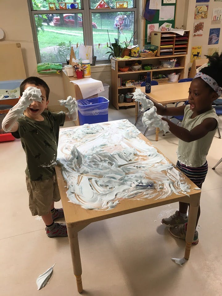 Two children playing with shaving cream on a table in a classroom