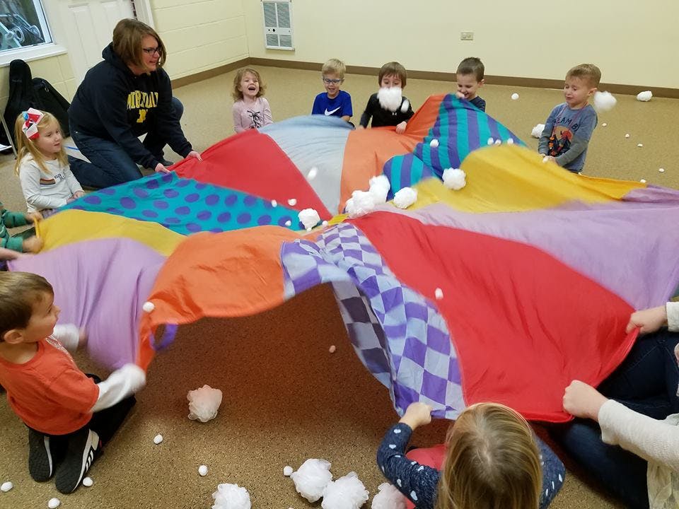 Adult and children playing with a colorful parachute and white balls