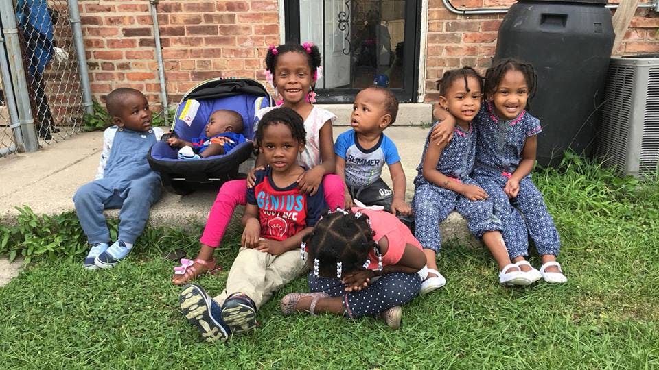 Seven children and a baby in a car seat sitting on grass