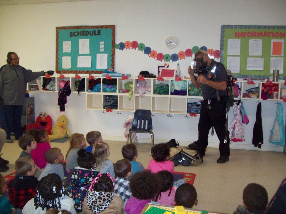 Two adults presenting to a group of children sitting on the floor in a classroom