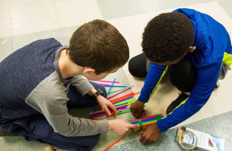 Two children on the floor working with colorful straws