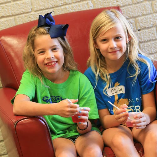 Two children sitting on a red couch holding cups with straws