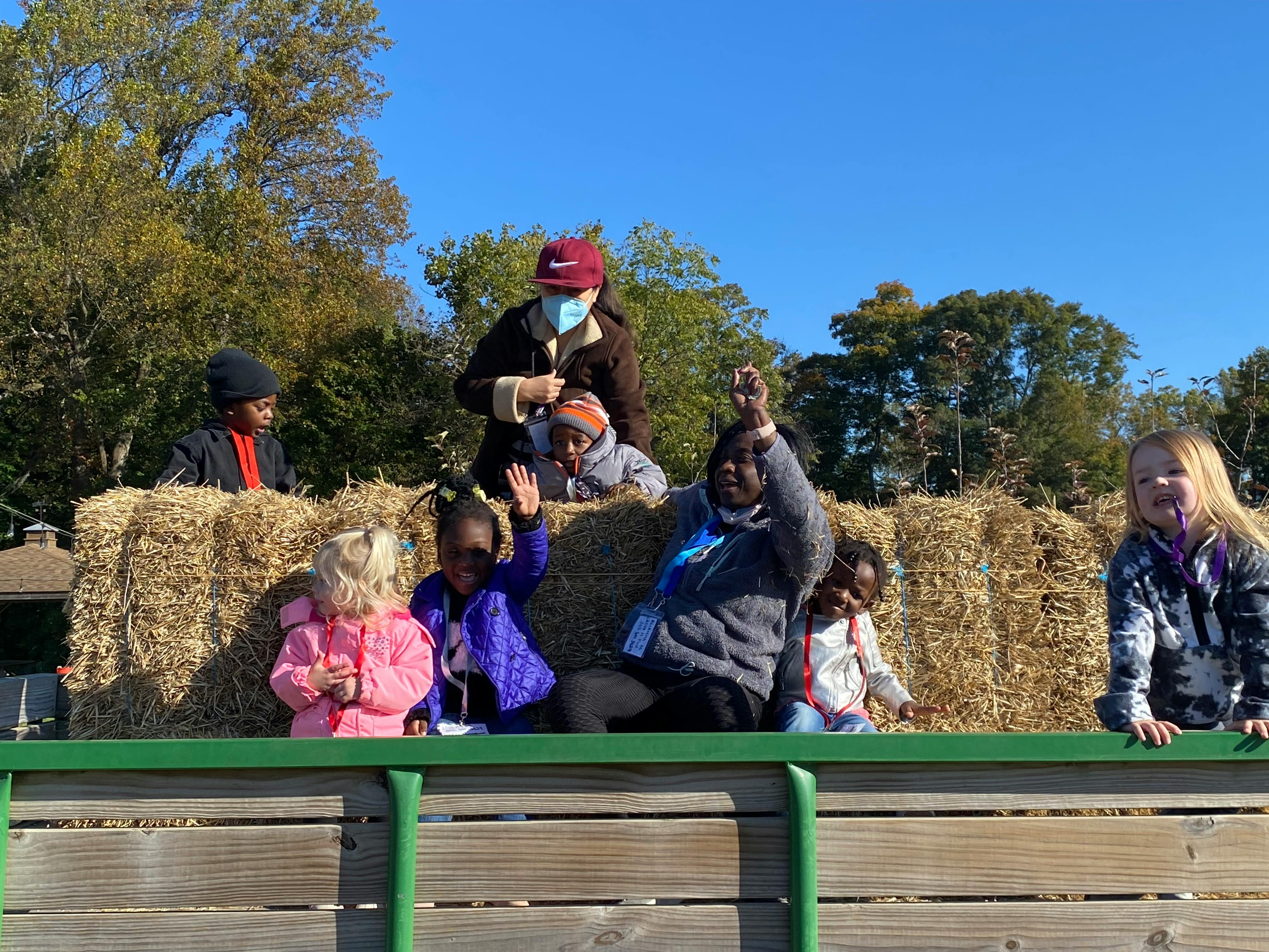 Children sitting on hay bales in a wagon, looking at the camera