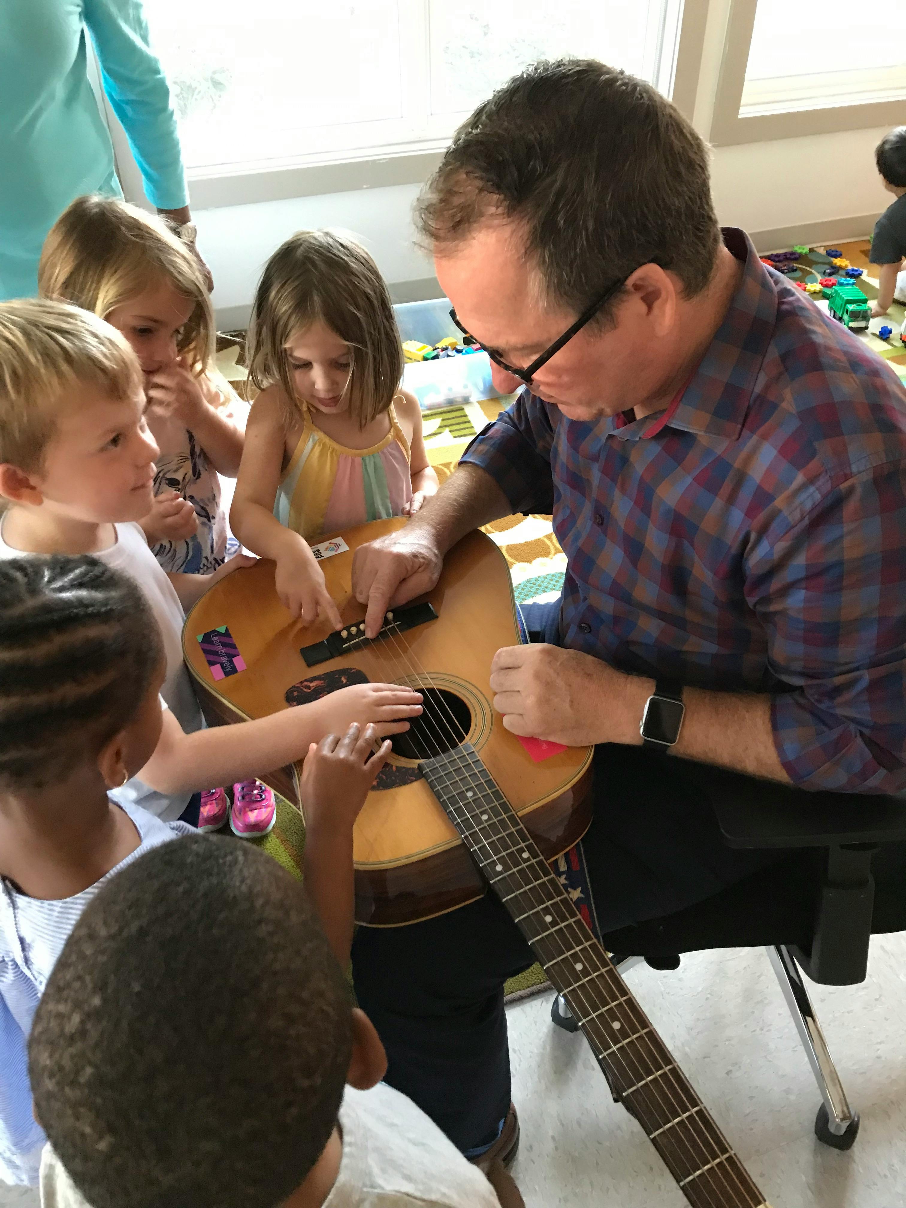 Adult playing guitar with several children gathered around
