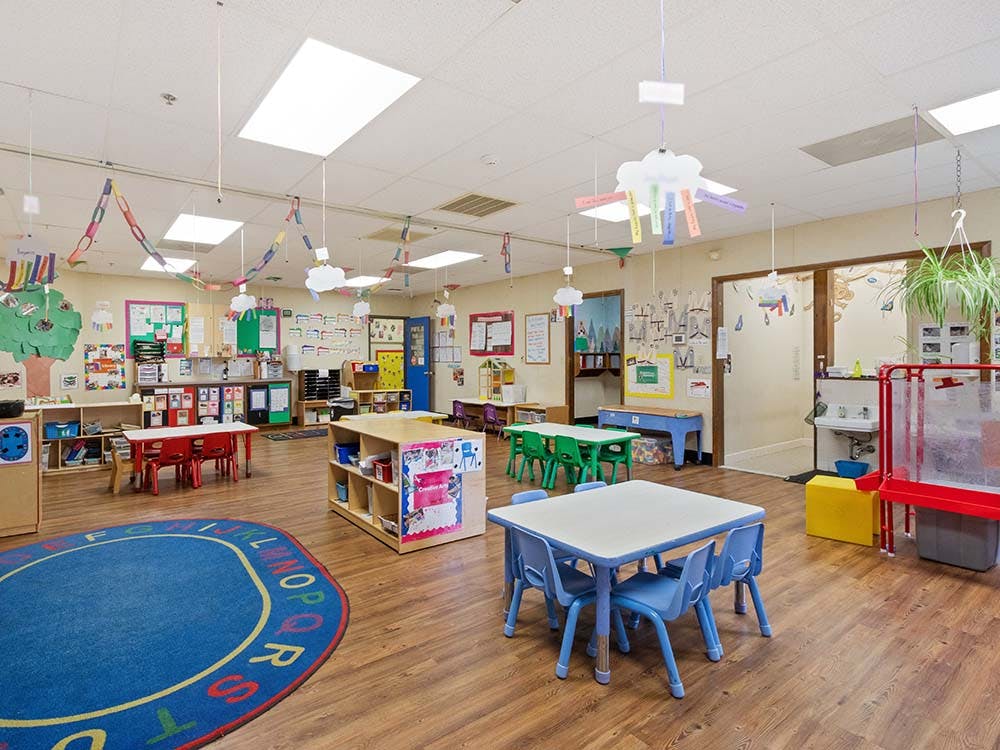 Colorful classroom with small tables and chairs, a blue rug, and wall decorations