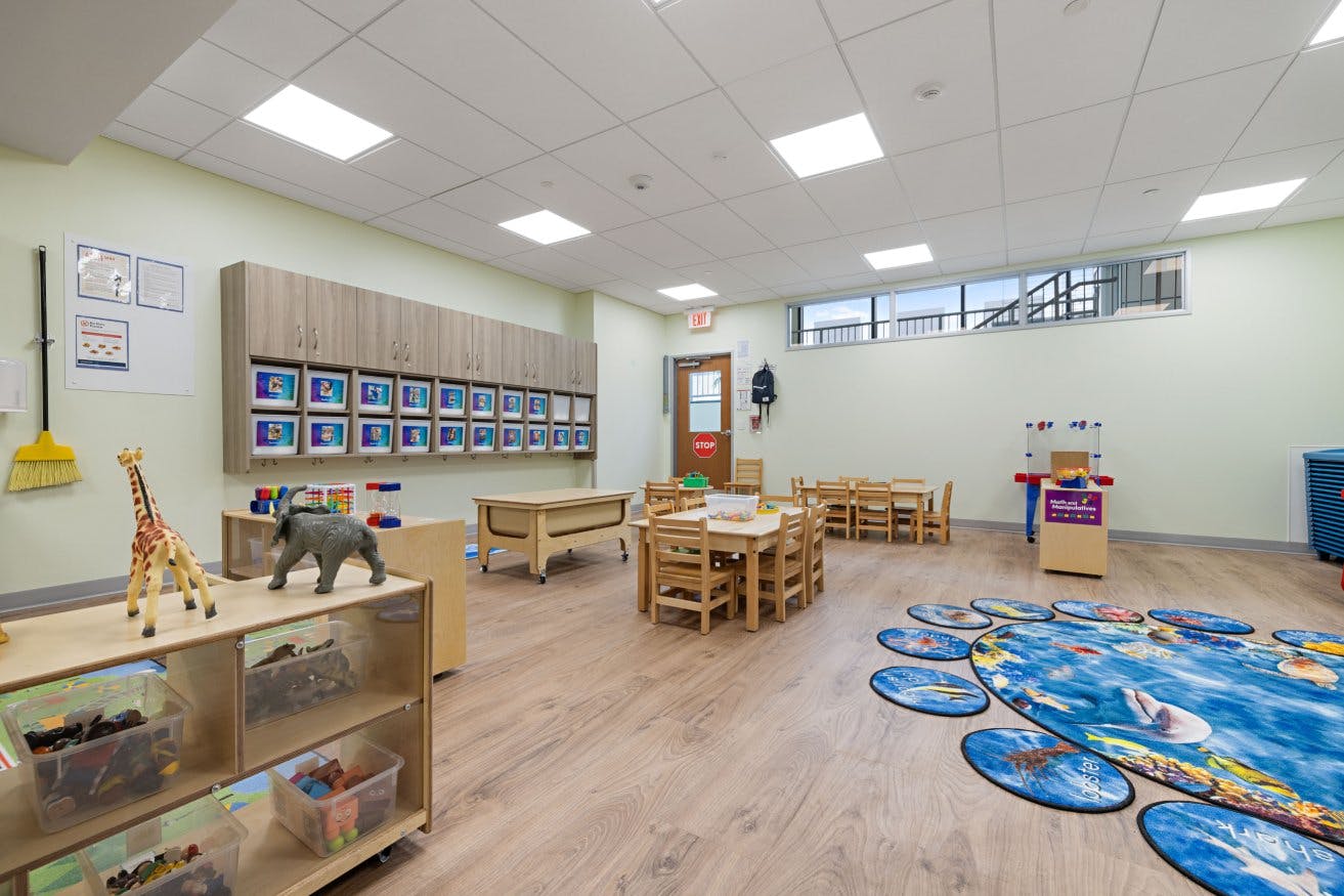 Empty classroom with small tables, chairs, storage, and a colorful rug