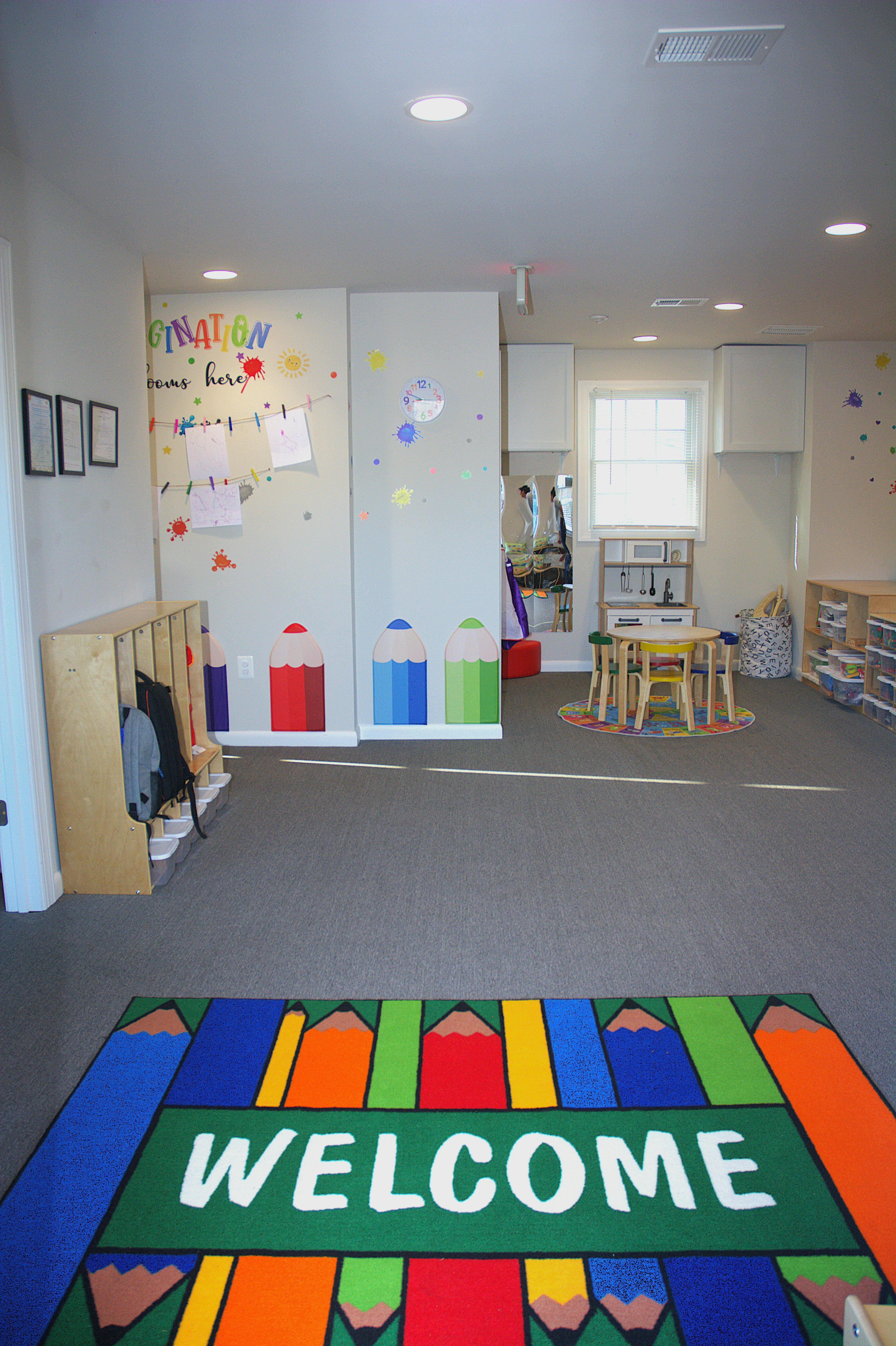 Classroom with a colorful WELCOME rug, small table and chairs, and cubbies