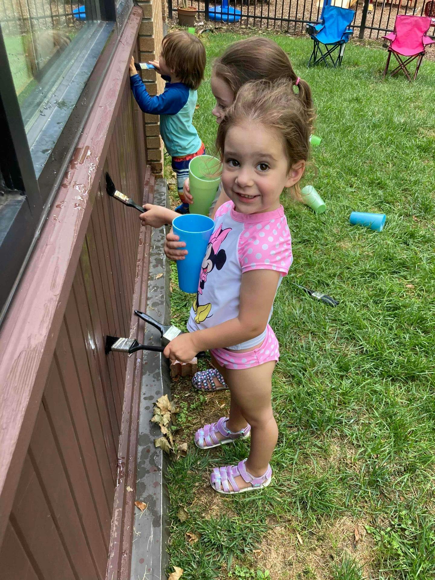 Children painting a brown wall outdoors