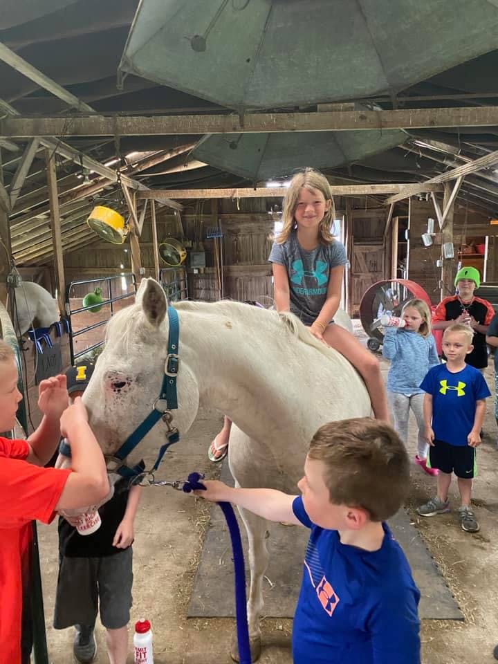 Child riding a horse while other children stand nearby