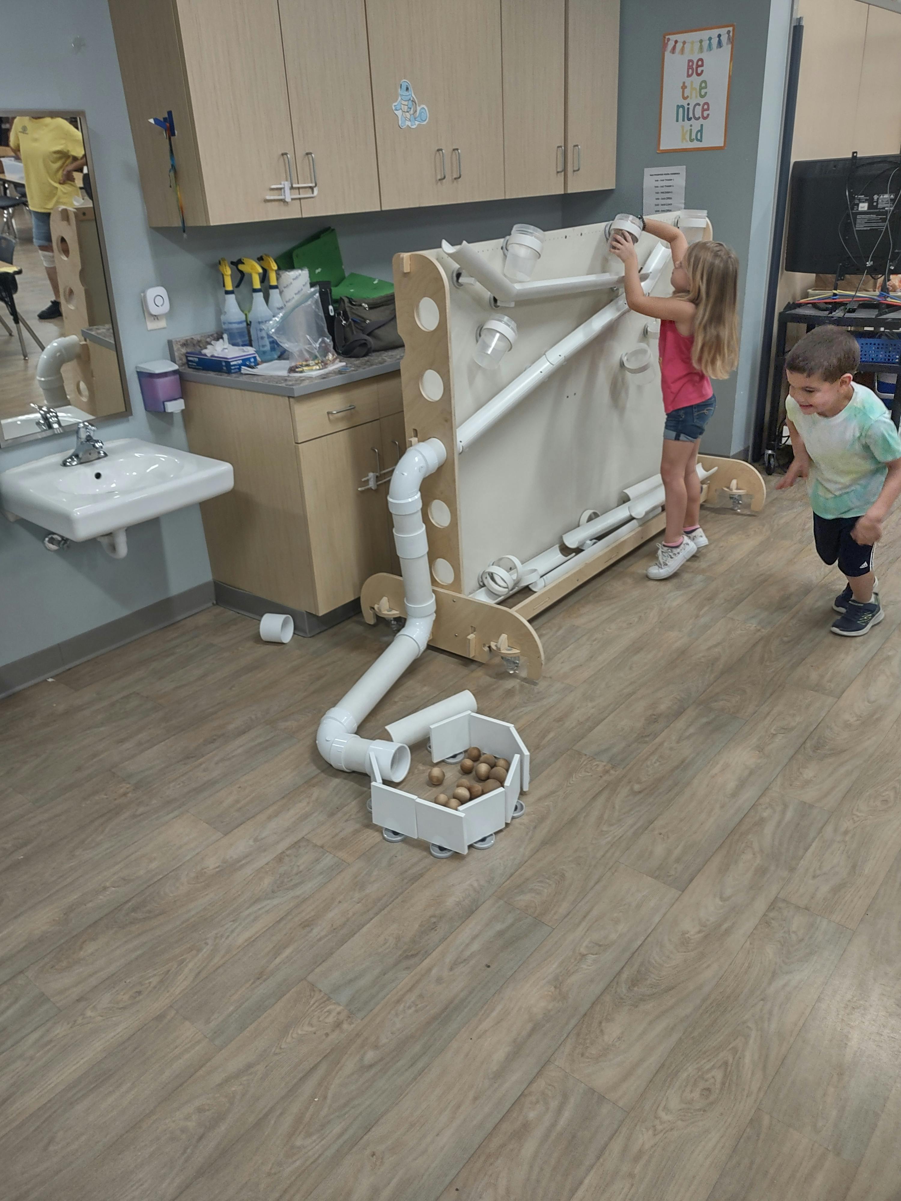 Child playing with a ball run toy, another child watching