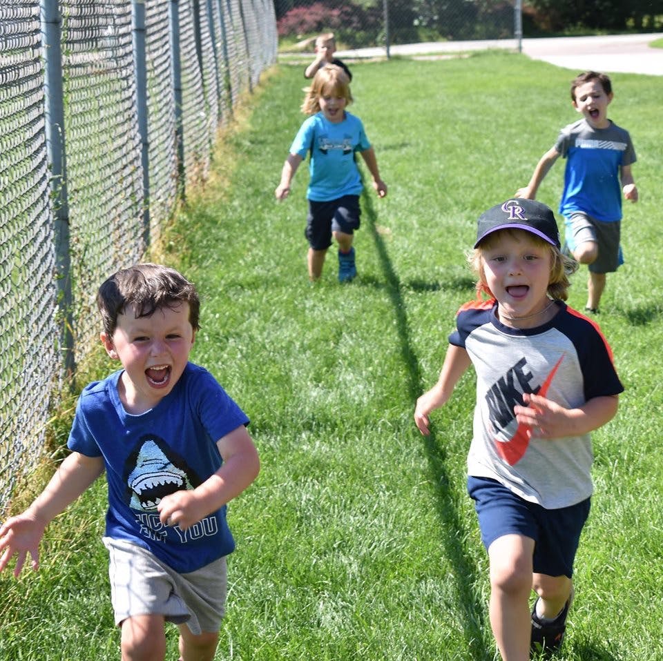 Children running on grass next to a fence
