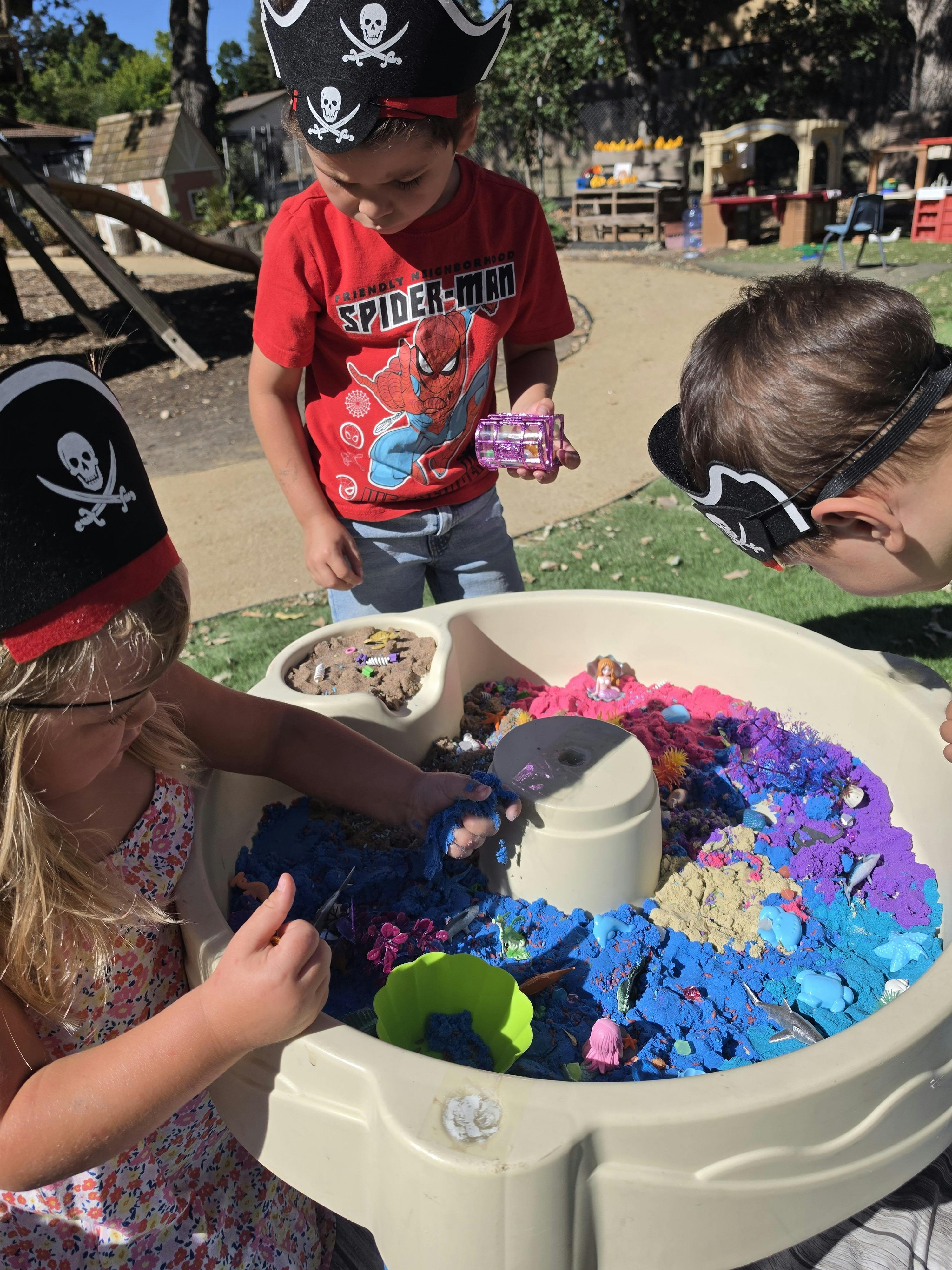 Children wearing pirate hats playing with colored sand in a sensory table