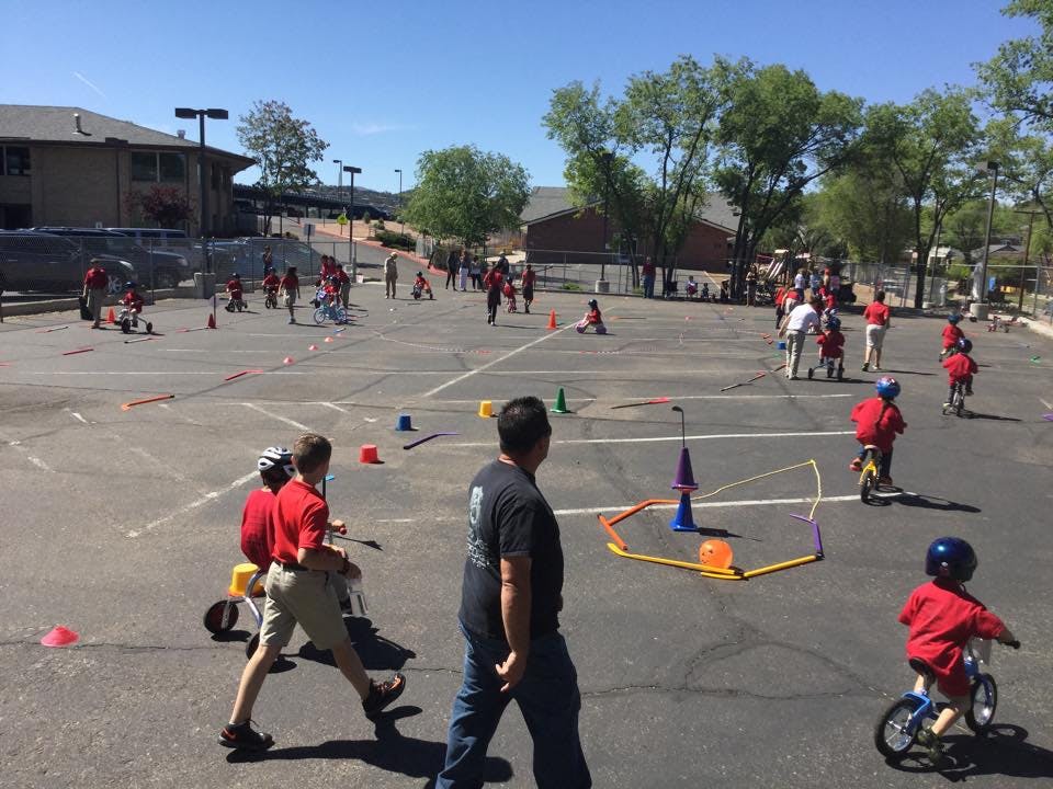 Children and adults on bikes and scooters in a paved area with cones