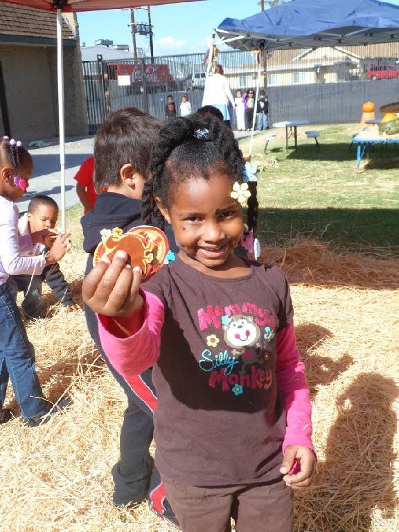 Child holding up a craft item, surrounded by other children and hay
