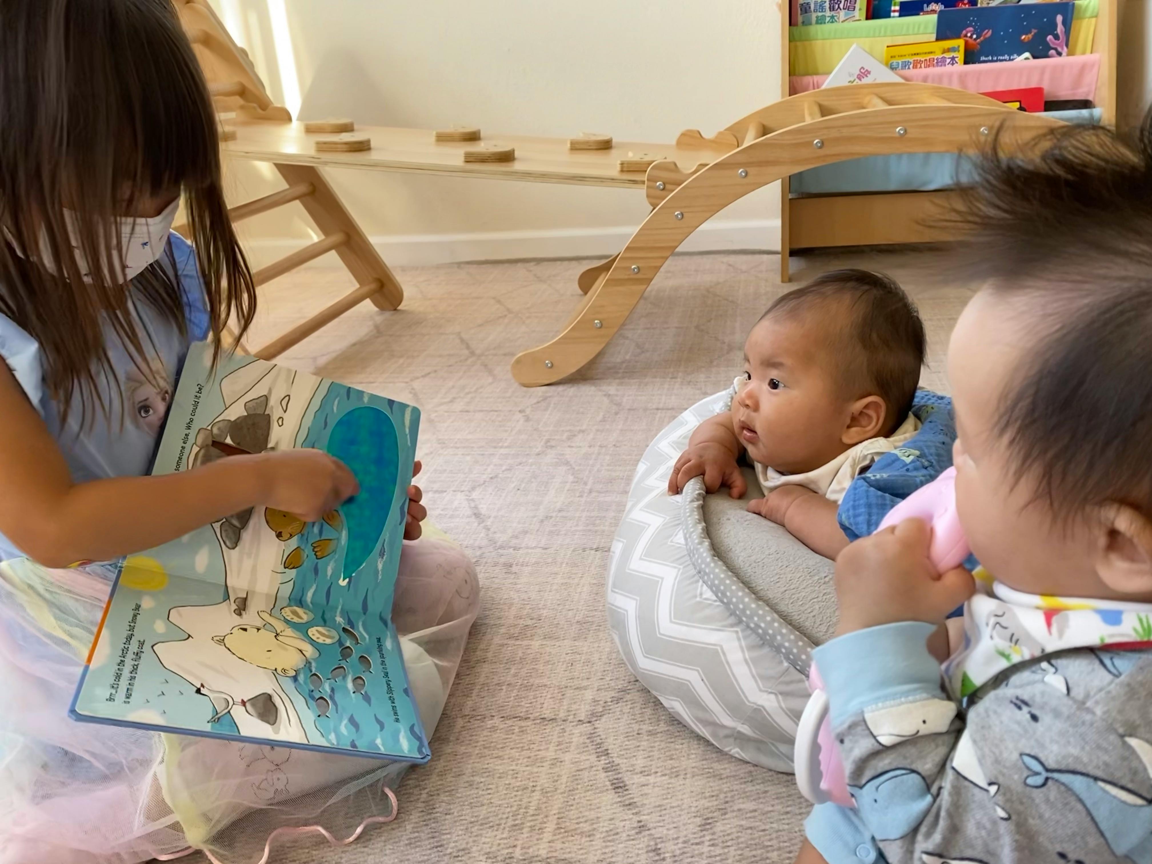 Child reading a book to two babies