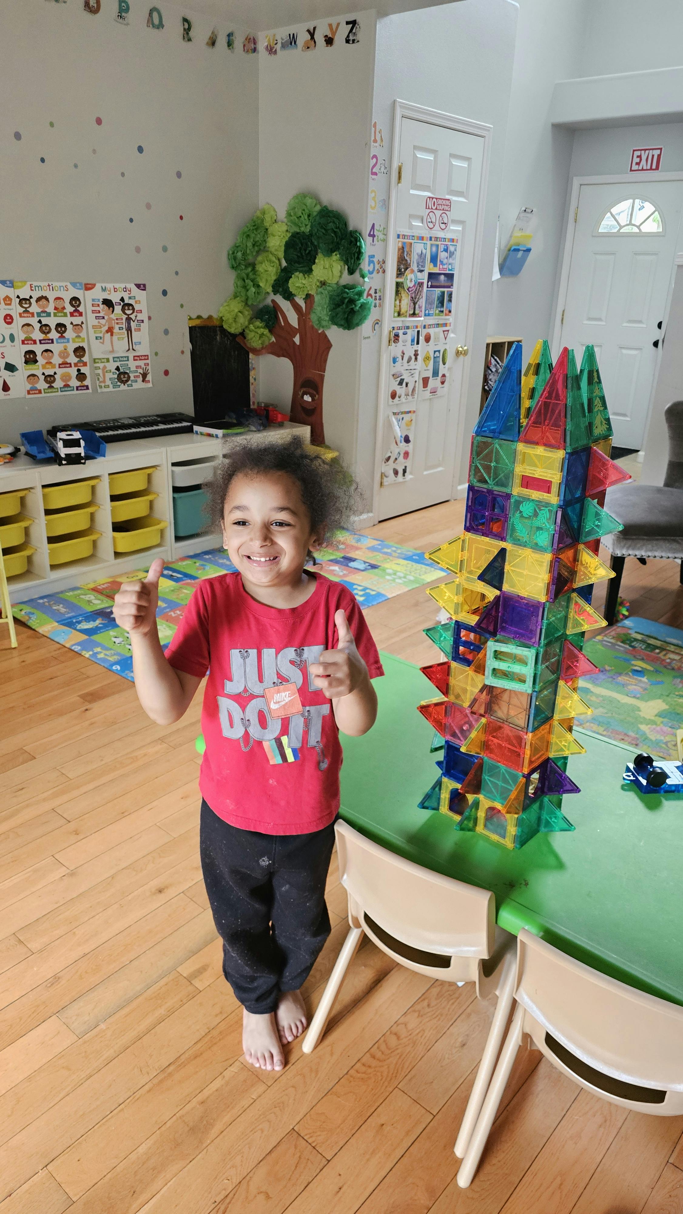 Child giving two thumbs up next to a tall colorful block tower