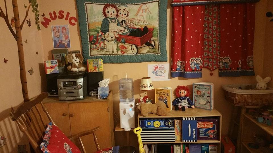Room with a stereo, water cooler, and bookshelf with a quilt and curtains