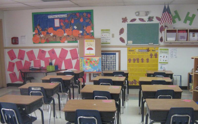 Empty classroom with student desks facing a front wall decorated with teaching materials