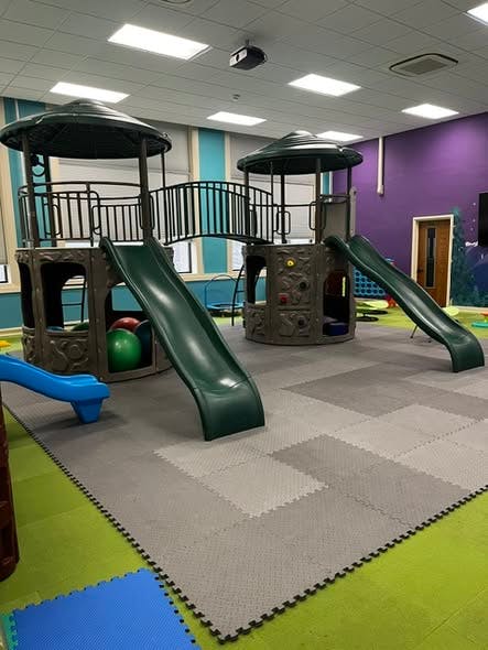 Indoor playground with two play structures connected by a bridge and slides