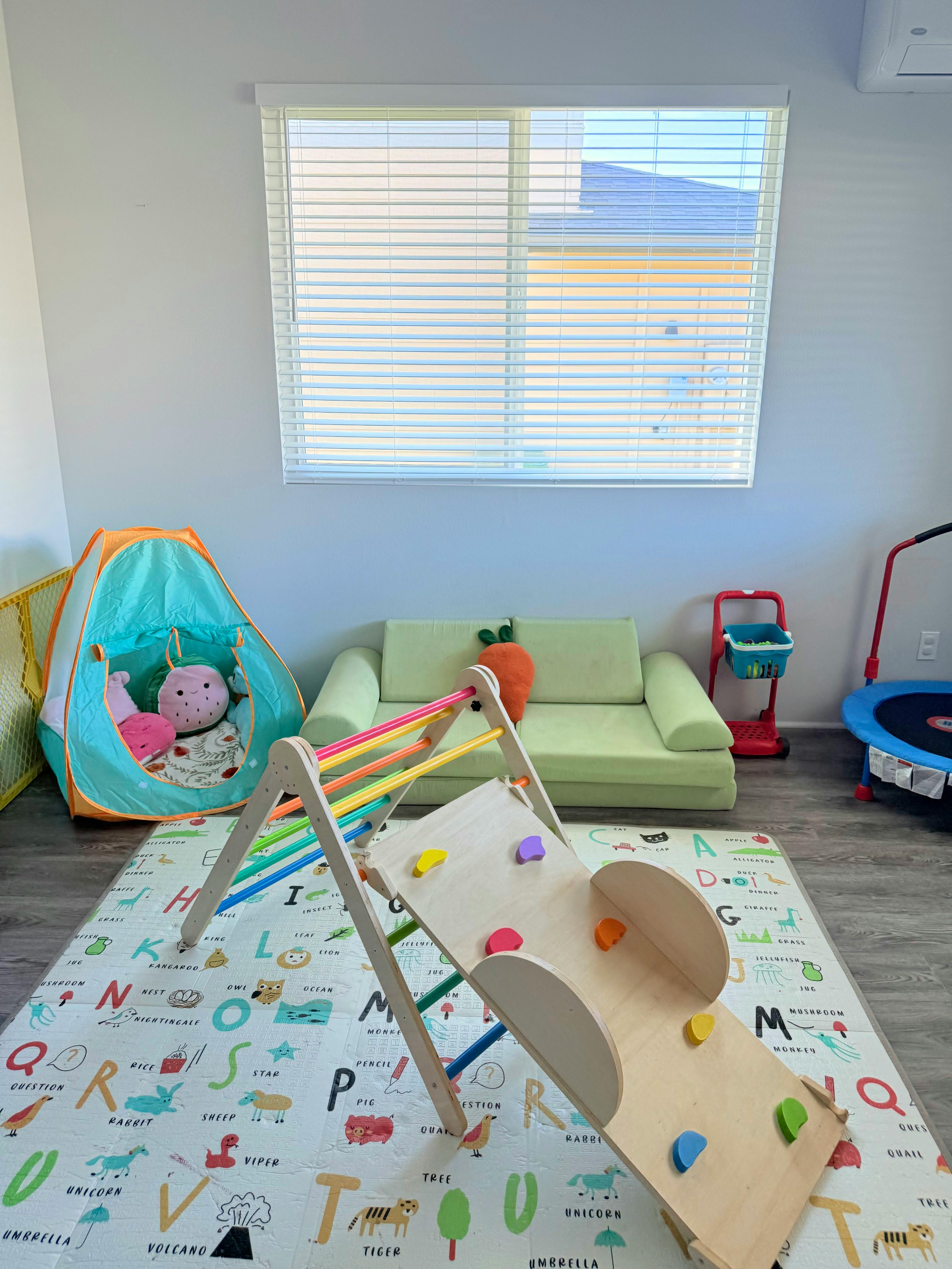 Indoor play area with a climbing structure, tent, and green sofa