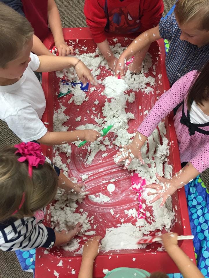 Children playing with kinetic sand in a red bin