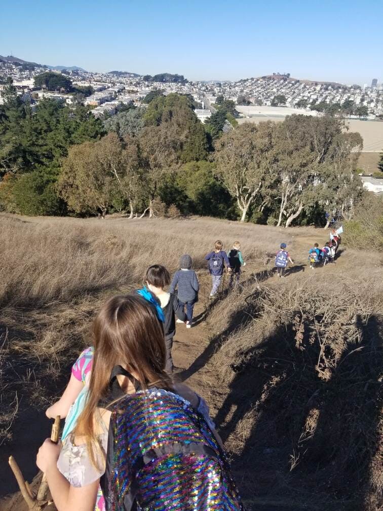 Children hiking on a dirt path with a city in the background